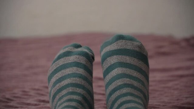 The man in the striped socks wiggles his fingers. Lying on a bed with a pink plaid blanket.