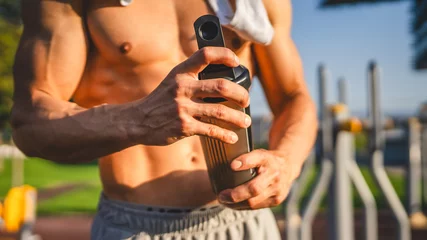 Zelfklevend Fotobehang One caucasian man young male athlete take a brake during outdoor training in the park outdoor gym hold supplement shaker in hand happy confident strong copy space © Miljan Živković