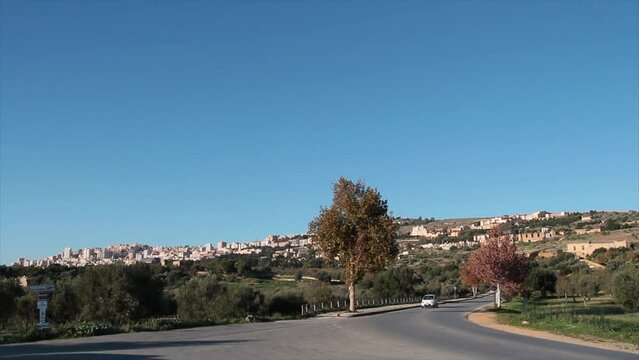 agrigento sicily italy road street entrance buildings homes houses on hill wide shot of city with car vehicle driving coming down