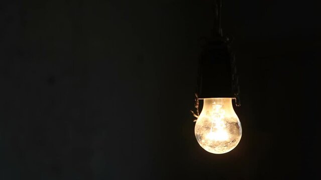 A man screws in a light bulb in a dark room.
