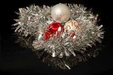 White and red Christmas baubles nested in a silver Christmas tinsel on a black background
