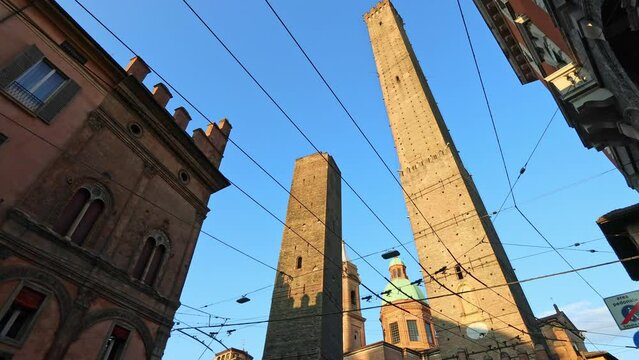 iconic Two Towers of Bologna in Italy. City's emblem against blue sky. Asinelli and Garisenda towers stand in historic city heart, with clock tower of Porta Ravegnana square adding to timeless charm.