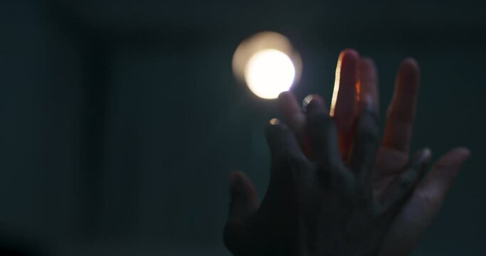White female hands and dar skinned man's hand together touching each ther dancing against the bright light in dark studio .