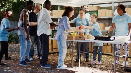 At charity food drive, volunteers share provisions and food with the homeless. Young people offer their time to feed the hungry among less fortunate, exhibiting the spirit of volunteerism. Handheld - obrazy, fototapety, plakaty