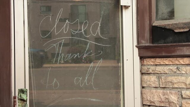 chalk writing closed thanks to all on chalkboard inside down window storefront with cars vehicles passing in reflection with brick and window next to it