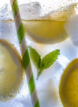 Cross section of cold drink with lemons, mint, straw, ice cubes