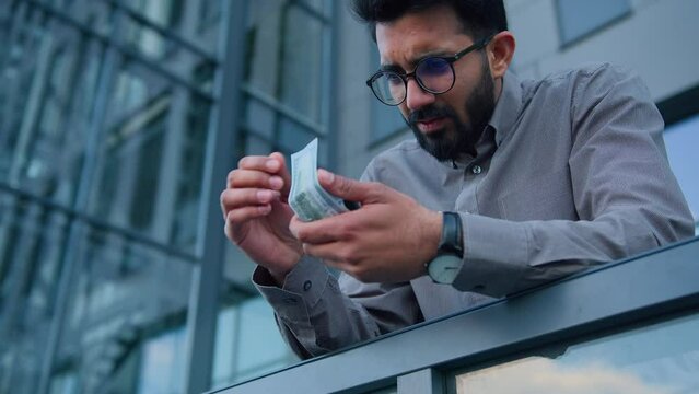 Indian Arabian upset poor man counting money cash calculate earnings income profit worried male businessman in city outdoors count dollars miserable salary problem financial crisis business inflation