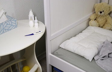 Flue medicine bottles and a thermometer on white table near bed with teddy bear in baby room