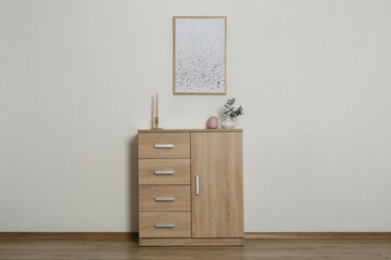 Chest of drawers, decorative elements and frame in room with light wall. Interior design