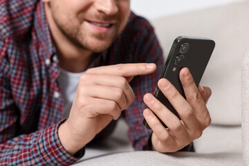 Man sending message via smartphone on sofa indoors, closeup