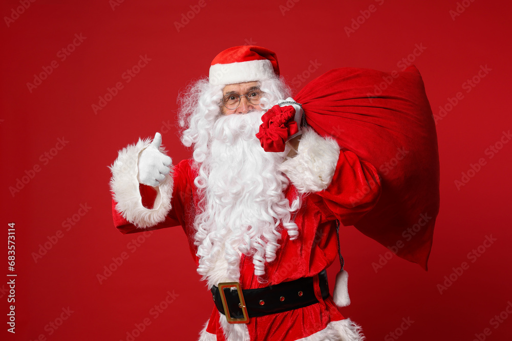 Sticker Santa Claus with bag of Christmas presents showing thumbs up on red background