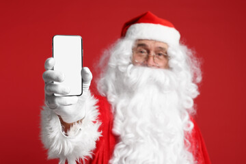 Merry Christmas. Santa Claus showing smartphone on red background, selective focus. Mockup for design