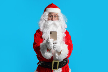 Merry Christmas. Santa Claus using smartphone on light blue background