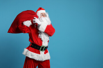 Santa Claus with bag of Christmas gifts on light blue background, space for text
