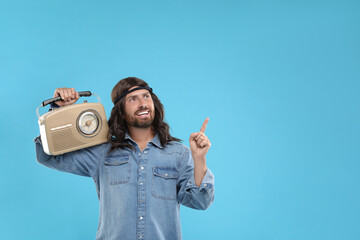 Stylish hippie man with retro radio receiver pointing at something on light blue background, space...