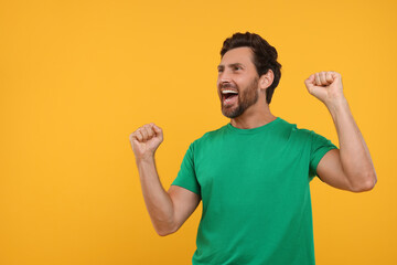 Emotional sports fan celebrating on orange background, space for text