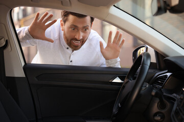 Automobile lockout, key forgotten inside. Emotional man looking through car window