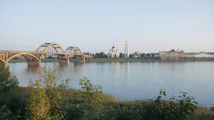 Beautiful bridge crossing wide river. Creative. City with a big church and green bushes.