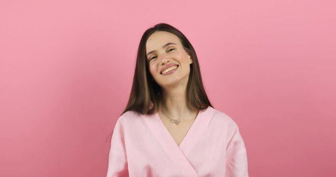 Portrait of young sexy playful brunette girl wear pink dress posing looking camera chewing bubble gum and pulling it out of teeth with fingers isolated on pink wall background in studio.