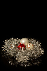 White and red Christmas baubles nested in a silver Christmas tinsel on a black background