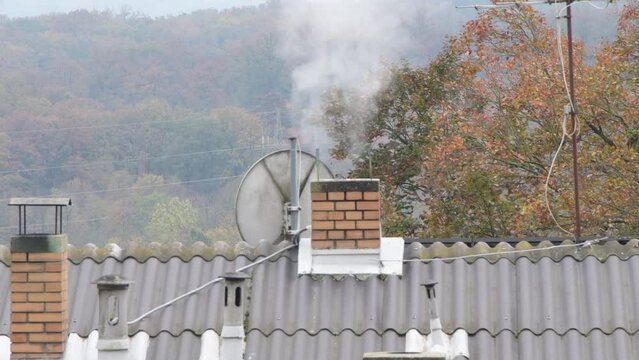 Smoke rises from a chimney on the roof of a house 