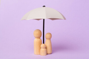 Wooden family figures with umbrella on color background