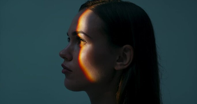 Young female in profile standing in studio isolated in bright light looking up playing with light dansinc with hands. Multicolour future of advertisement concept futuristic time.