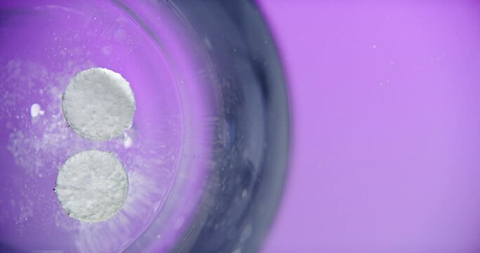 Medicine, glass and above of effervescent pills in water for health, medication and vitamins in studio. Healthcare, pharmacy and liquid with tablet, painkiller and paracetamol on purple background