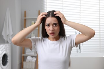 Emotional woman examining her hair and scalp in bathroom. Dandruff problem