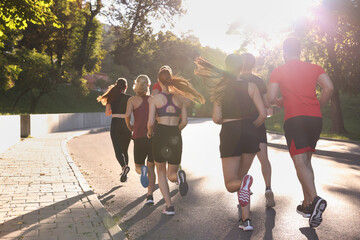 Group of people running outdoors on sunny day, back view