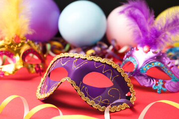 Beautiful carnival mask and party decor on red table, closeup