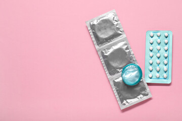 Condoms and birth control pills on pink background, flat lay and space for text. Choosing method of contraception - obrazy, fototapety, plakaty