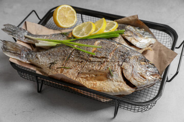 Seafood. Delicious baked fish served with green onion and lemon on light textured table, closeup