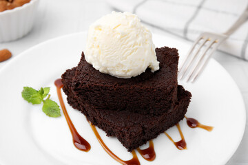 Tasty brownies served with ice cream and caramel sauce on white table, closeup