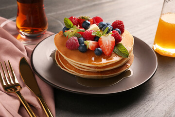 Delicious pancakes with fresh berries, honey and butter served on grey table, closeup