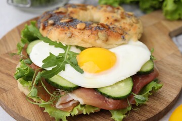 Tasty bagel with cured ham, egg, cucumber and salad mix on table, closeup