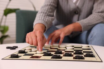 Woman playing checkers at white table indoors, closeup