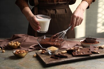 Woman with glass of milk and whisk mixing delicious chocolate cream at textured table, closeup