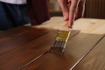 Man with brush applying wood stain onto wooden surface, closeup