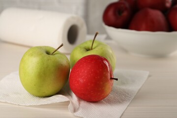 Fresh apples and paper towel on light wooden table, closeup