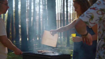 Friends cook meat on coals with grill. Stock footage. Woman blows up coals for grilling meat. Woman...