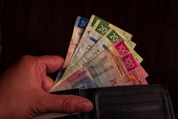 Hand holding a wallet with Mexican bills of different denominations.