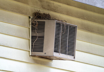 old air conditioner installed on old wood wall building with bird nest