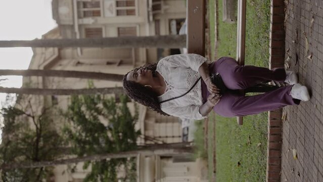 Linda mulher negra, sentada no banco da praca, sorrindo. Cinematico 4k. Video vertical.