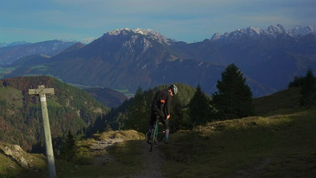 Male cyclist on gravel bike enjoying view and making phono on phone on top of mountain in alps with beautiful view of snowy peaks of mountain range in germany. Sports motivation and inspiration. 