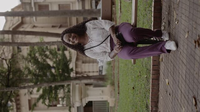 Linda mulher negra, sentada no banco da praca, sorrindo. Cinematico 4k. Video vertical.