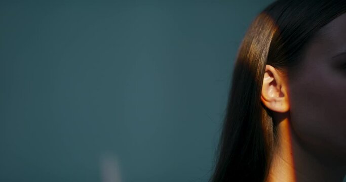 Close up shot part of body in front of light in the studio isolated. Brunette young woman with dark long hair in orange colourful lights .