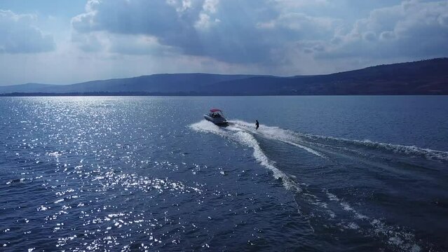 men wakeboarding on the lake while speed boat drag him on cloudy winter day and sun flares shine through the clouds