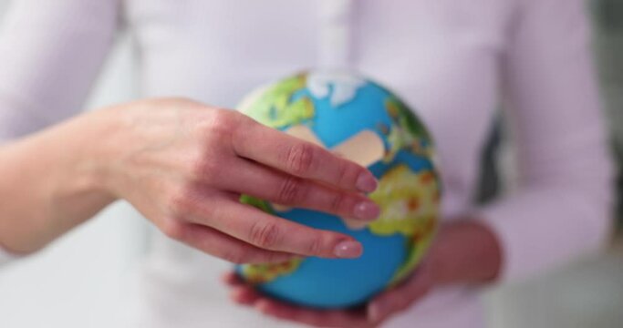 Woman holding globe of planet Earth with adhesive plaster