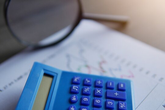 Closeup image of calculator, magnifying glass and line graph. Data and finance analysis, business intelligence and trends concept.
